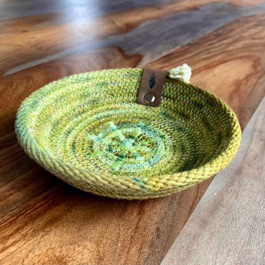Small green colored rope basket from Astile Lane, shown on woodgrain surface.