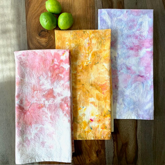 Three colorful kitchen towels on a wooden surface with limes.