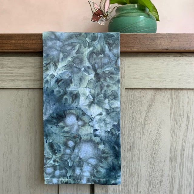 Marble-patterned kitchen towel on a wooden surface with a plant in the background